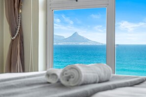 Una cama con toallas enrolladas y una ventana con vista a la montaña y al océano.