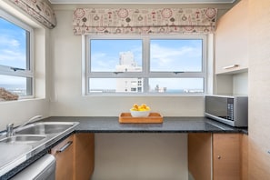 Cozinha com pia dupla, micro-ondas e janela com vista para prédios.