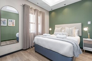 Une chambre à coucher moderne avec un lit, une table de chevet, une lampe et un grand miroir.