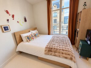 Une chambre à coucher avec un lit, une fenêtre avec des rideaux, une armoire en bois et un tableau encadré au mur.