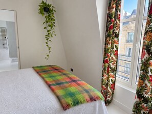 Une pièce avec un lit, une plante suspendue et une fenêtre ornée de rideaux à motifs floraux.