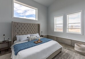 Ein Schlafzimmer mit einem großen Bett, zwei Nachttischen, einem Fenster mit Jalousien und Blick ins Freie.