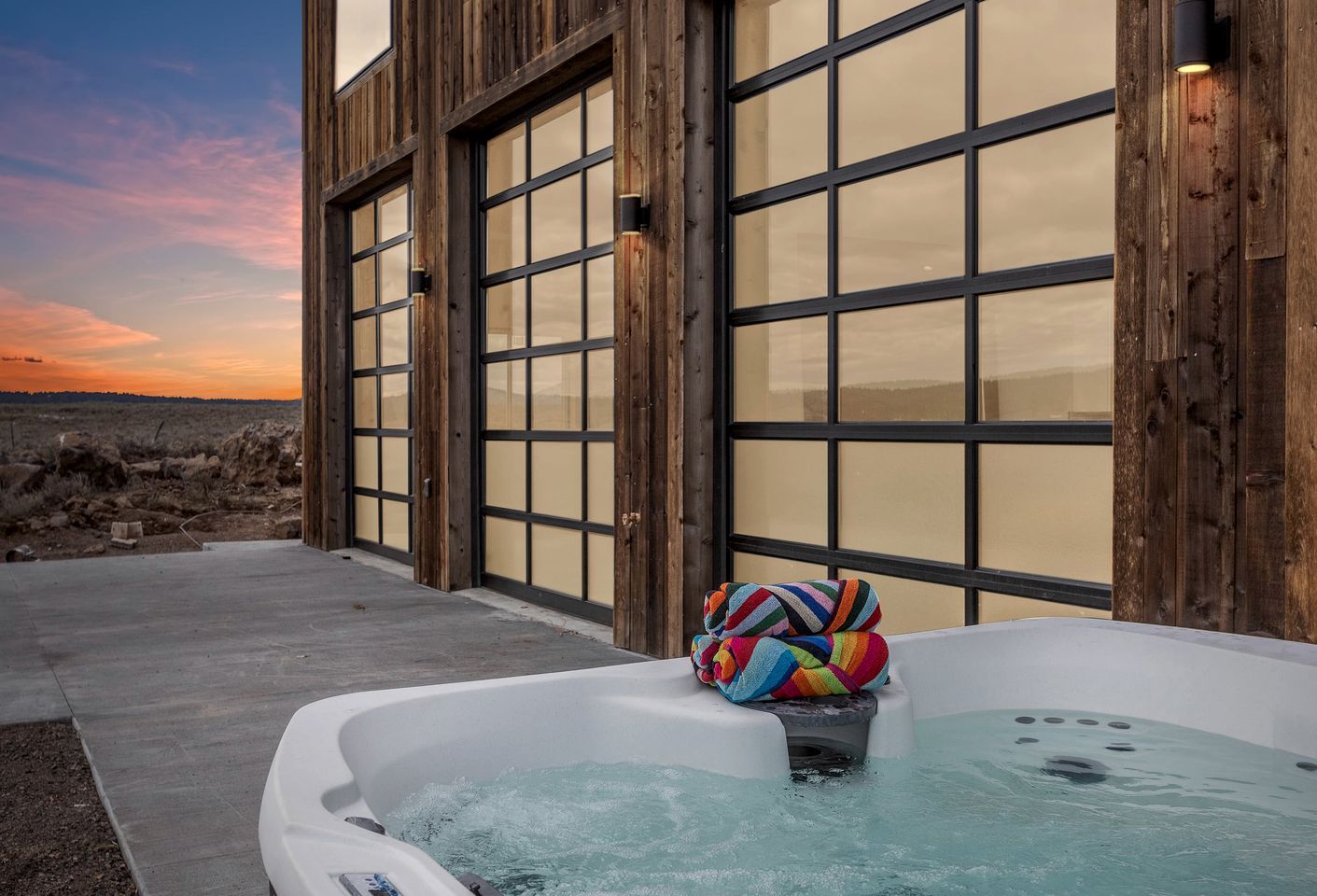 A hot tub with a colorful towel beside it, set against a building with large windows and a view of the beach.