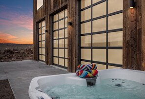 Ein Whirlpool mit einem bunten Handtuch daneben, vor einer Gebäudes mit großen Fenstern und Blick auf den Strand.