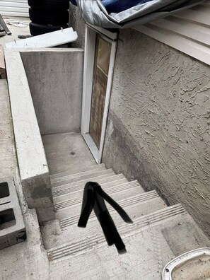 Un escalier en béton menant à une porte dotée d’une fenêtre, le tout entouré d’un mur à texture.