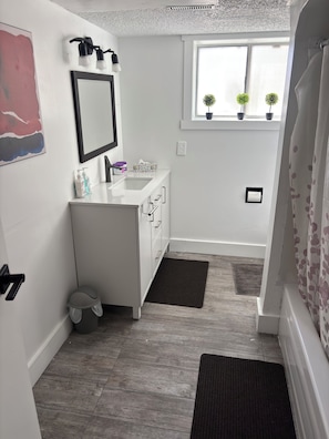 Une petite salle de bain avec un lavabo blanc, un miroir et une fenêtre agrémentée de plantes en pot.