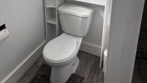 Un baño pequeño y blanco con inodoro, estante y mueble sobre el inodoro.
