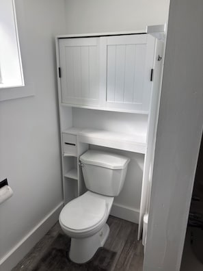 Een kleine, witte badkamer met een toilet, een plank en een kastje boven het toilet.