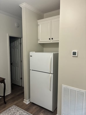 A kitchen with a white refrigerator, white cabinets, and a vent on the wall.