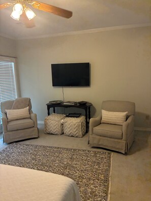 A living room with two armchairs, a flat-screen TV, a ceiling fan, and a patterned rug.
