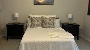 Quarto com cama, duas mesas de cabeceira, ventoinha no teto, quadro pendurado na parede e tapete estampado.