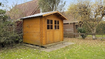 Un abri en bois avec une porte et des fenêtres, entouré d’herbe et d’arbres.