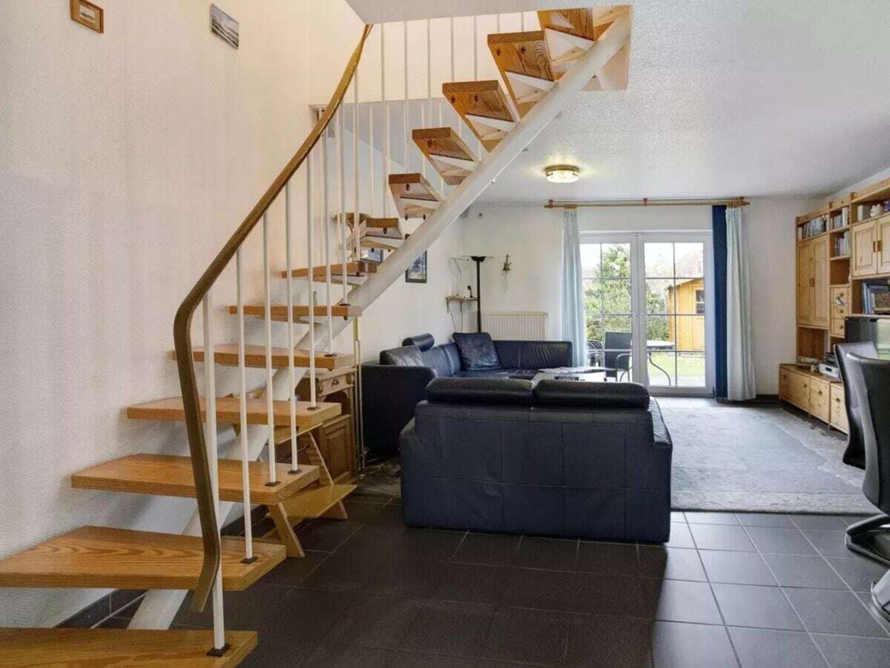 A modern living room with a wooden staircase, a dark-colored sofa, and a bookshelf.