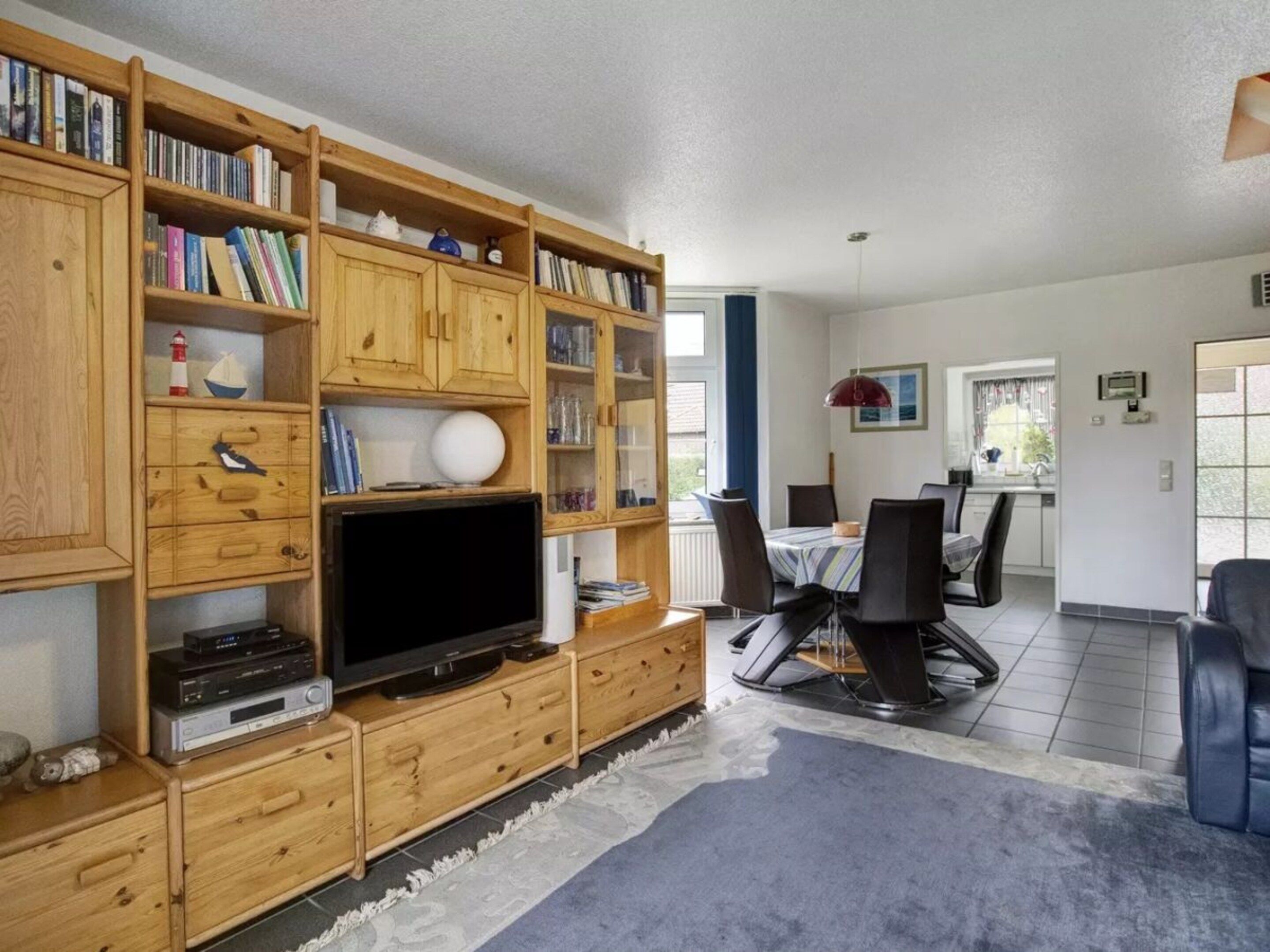 A living room with a wooden entertainment unit, a flat-screen TV, and a dining area with a table and chairs.