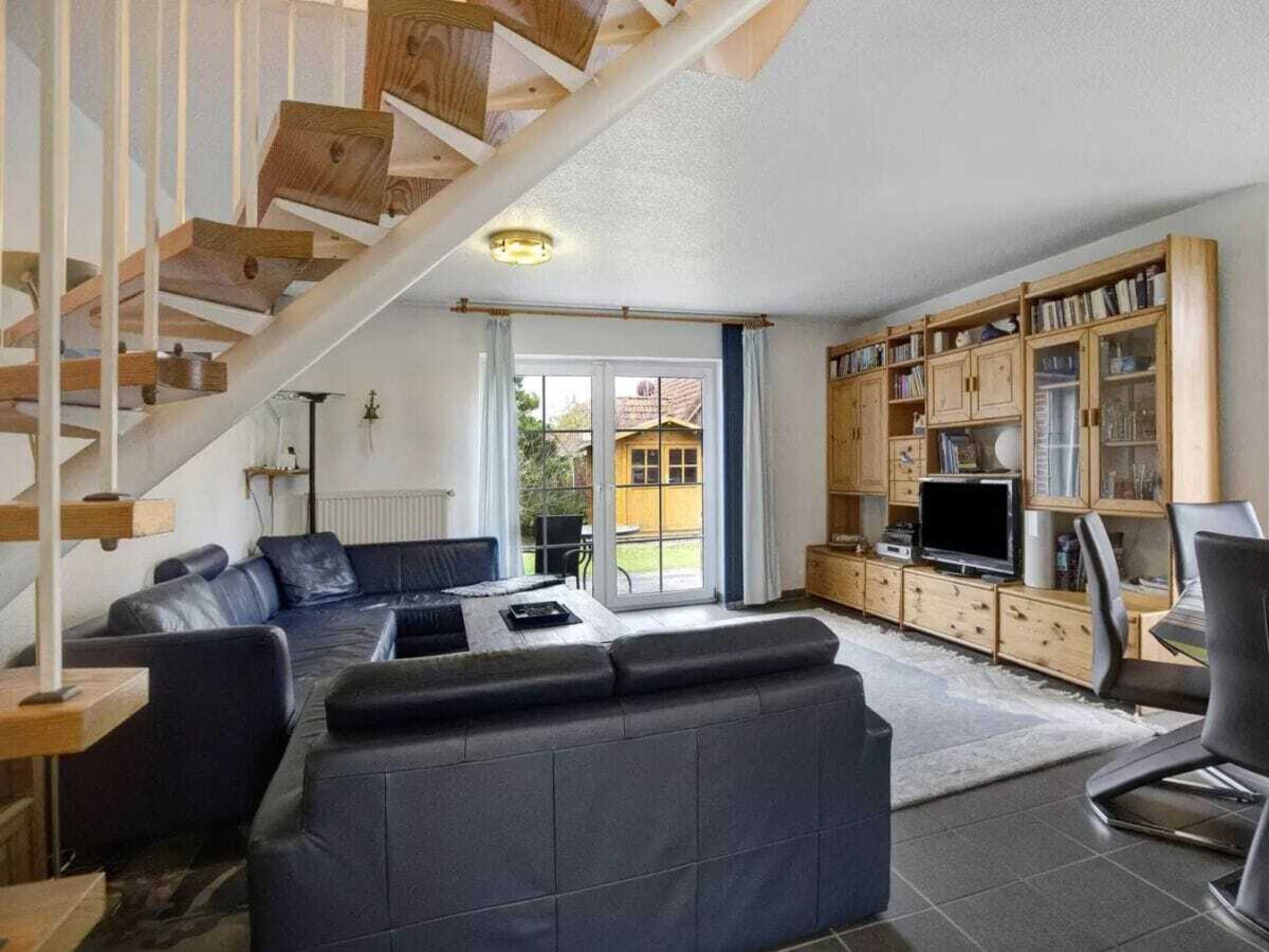 A living room with a sofa, a television, and a wooden staircase.