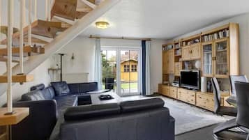 A living room with a sofa, a television, and a wooden staircase.