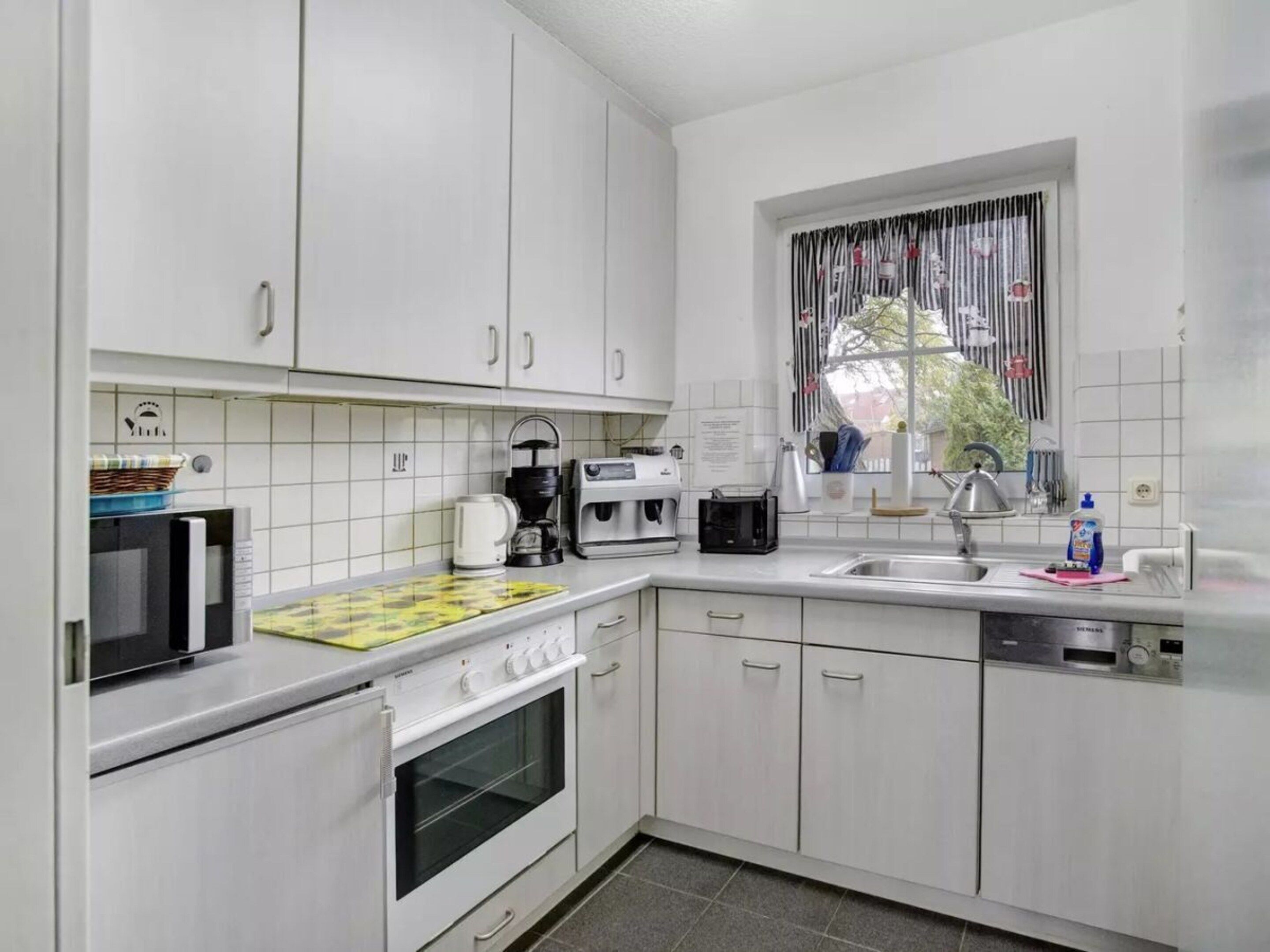 Een moderne keuken met witte kasten, een magnetron, een koffiezetapparaat, een broodrooster en een spoelbak.