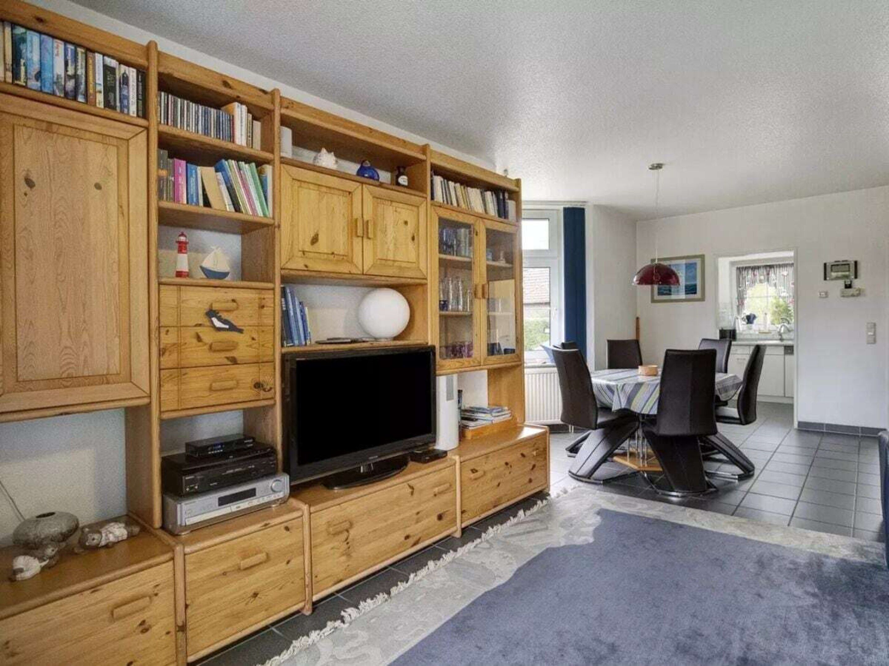 Un salon comprenant un meuble de rangement en bois pour les appareils multimédias, un téléviseur et un coin repas avec une table et des chaises.