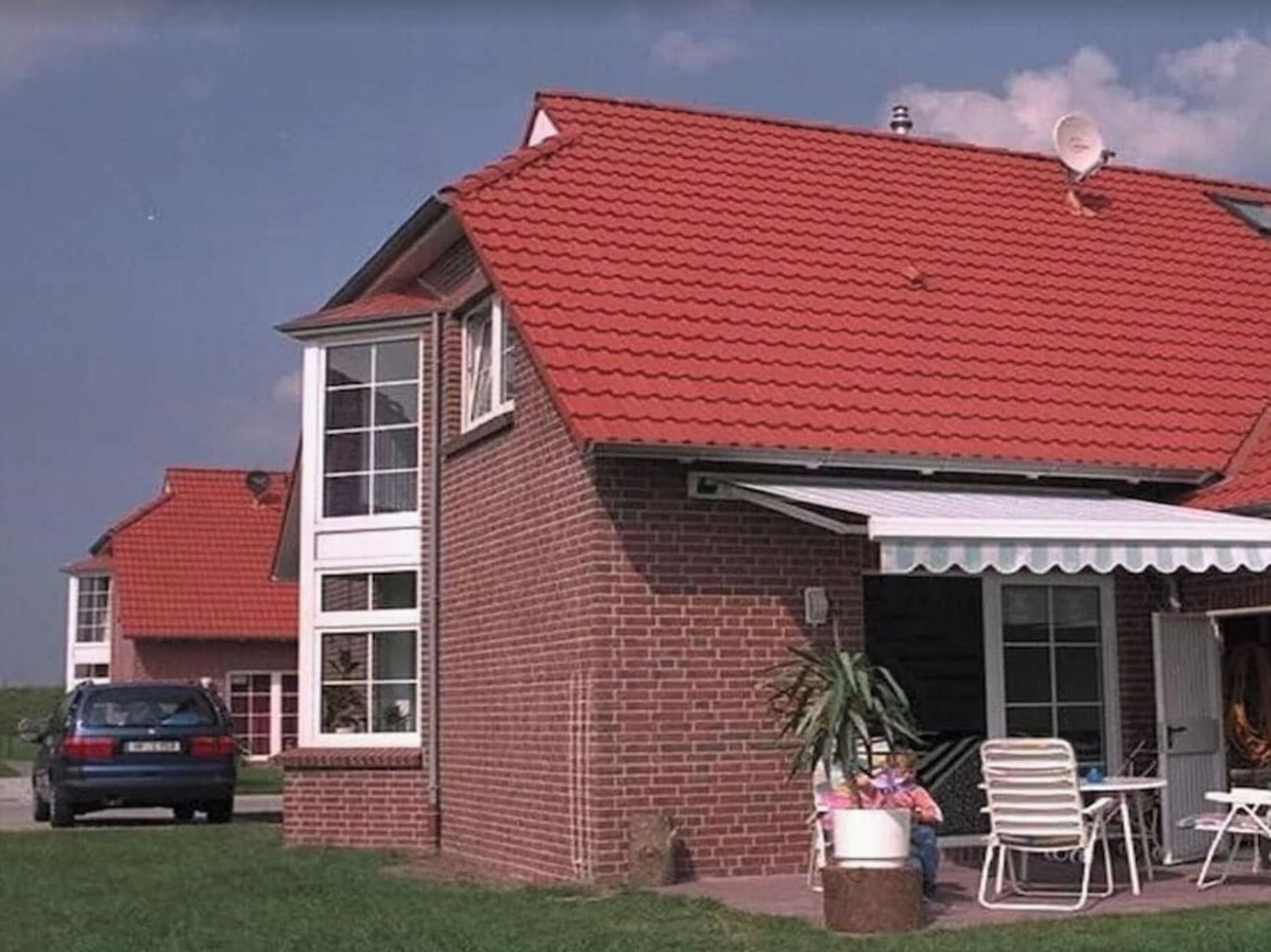 A two-story brick house with a red tiled roof, a satellite dish, and a covered patio area with outdoor furniture.