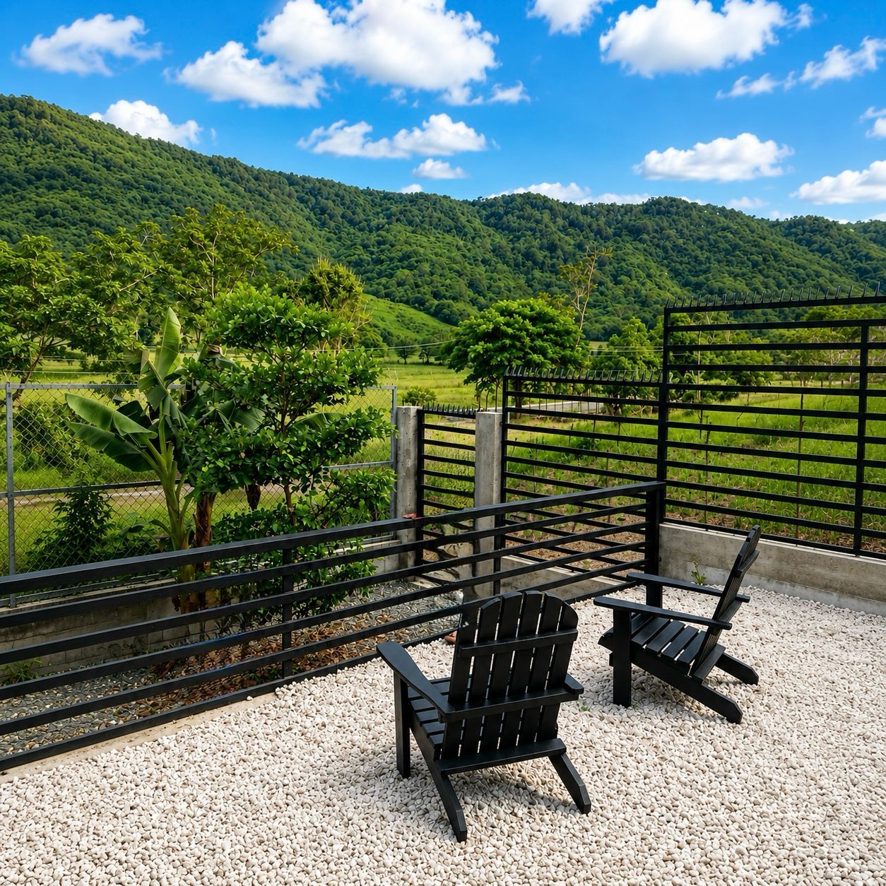 Una terraza con dos sillas Adirondack, una cerca de metal y vistas a un paisaje verde con colinas.