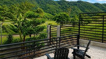 Una terraza con dos sillas Adirondack, una cerca de metal y vistas a un paisaje verde con colinas.