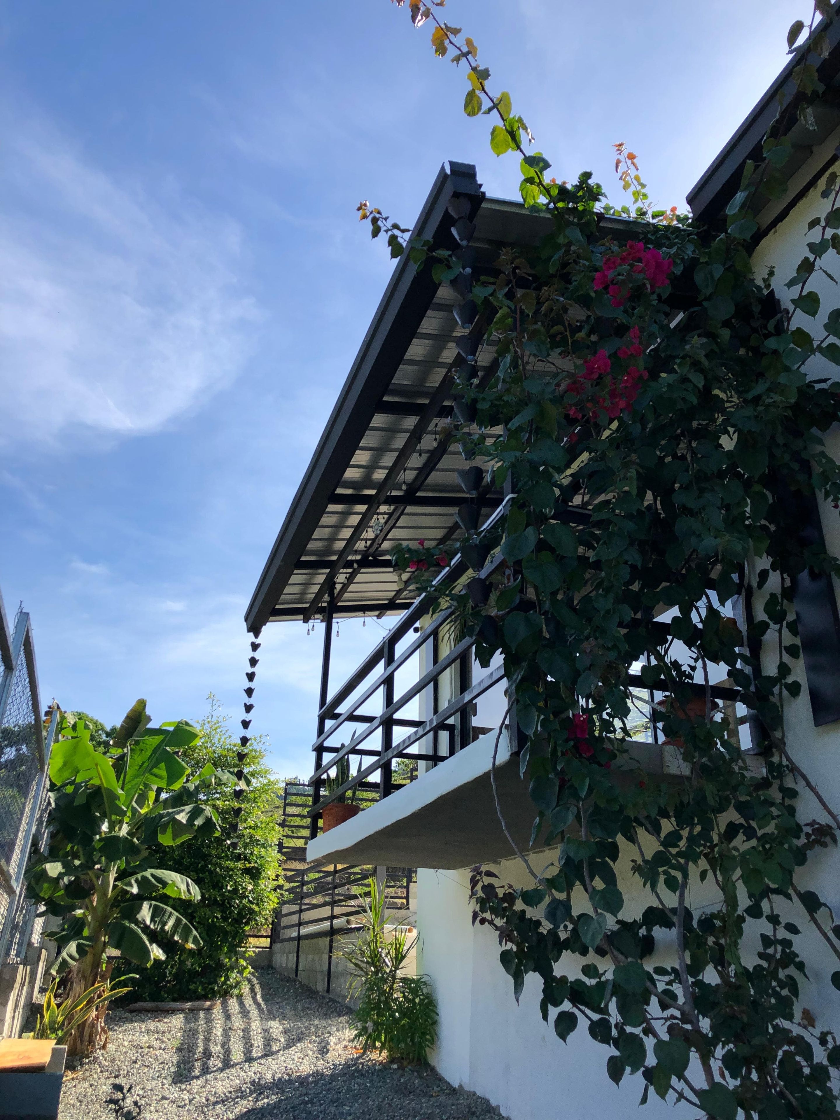 Un edificio con balcón, rodeado de vegetación y un cielo despejado.