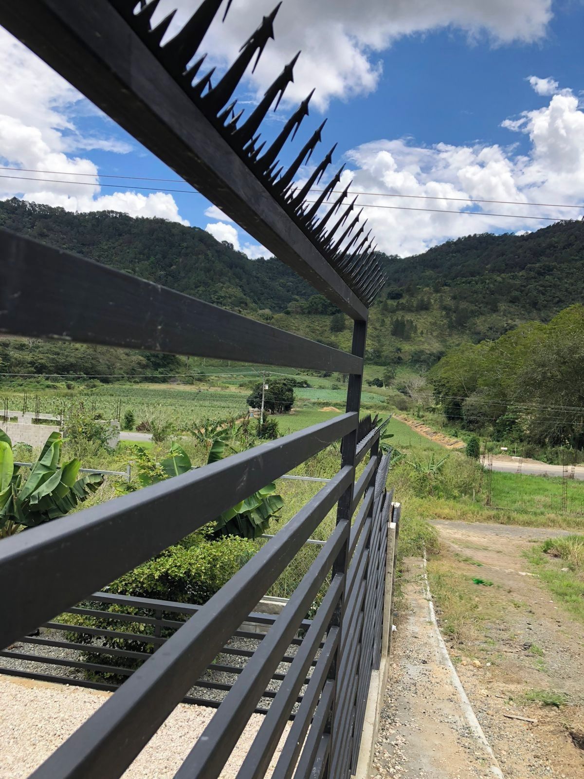 A metal railing with a view of a rural landscape, including fields and hills.