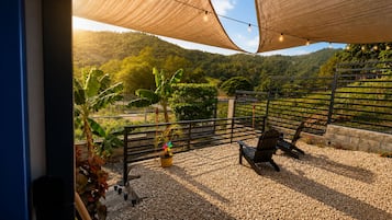 Un área de estar al aire libre con suelo de grava, cerca de madera y vista a un paisaje montañoso.