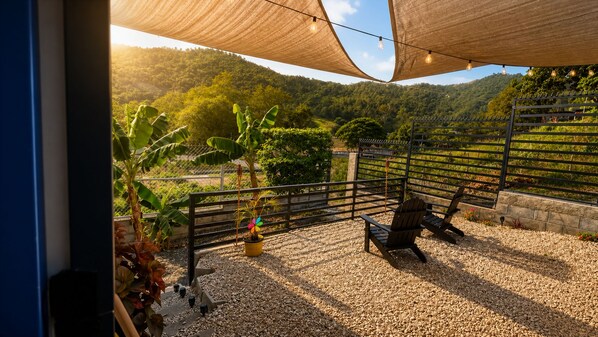 An outdoor seating area with a gravel floor, a wooden fence, and a view of a hilly landscape.