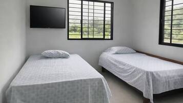 Habitación con dos camas individuales, un televisor de pantalla plana montado en la pared y ventanas amplias con vistas a zonas verdes.