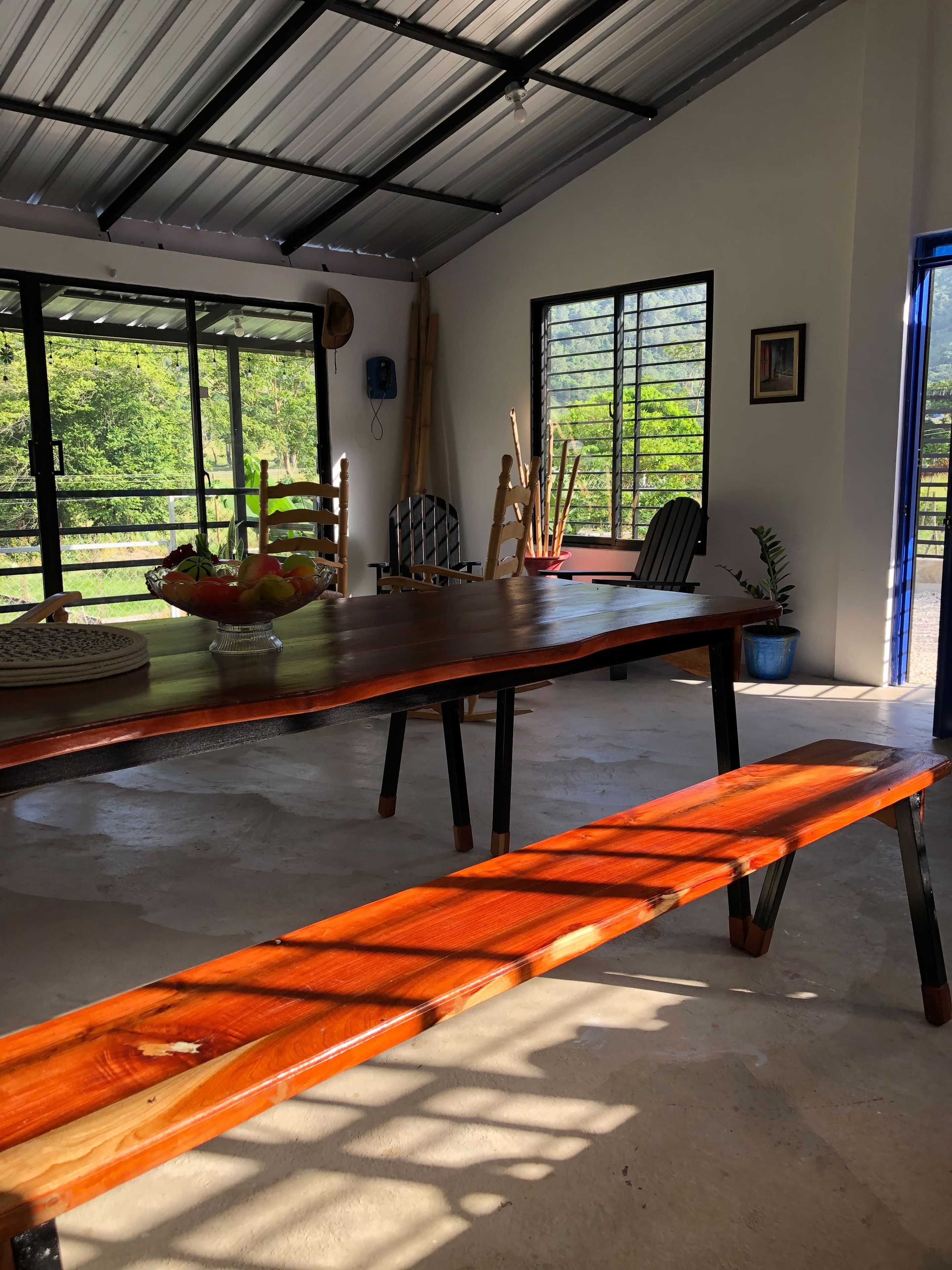Una habitación amplia con una larga mesa de madera, sillas, un banco y un ventanal con vistas a la vegetación.