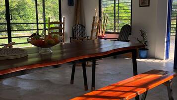 Una habitación amplia con una larga mesa de madera, sillas, un banco y un ventanal con vistas a la vegetación.