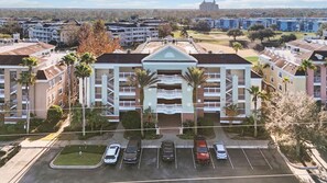 A multi-story hotel with a central courtyard, parking lot, and surrounding greenery. - 3BR Reunion Resort Condo With Golf Views, Pool, Wifi, and en Suite Bedrooms (Kissimmee)