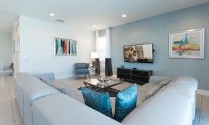 A modern living room with a light blue wall, a sofa set, a coffee table, a TV, and artwork. - 5BR Encore Villa Movie-themed Game Room (Kissimmee)