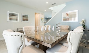 A dining area with a glass-top table, white upholstered chairs, and a staircase leading to another room. - 5BR Encore Villa Movie-themed Game Room (Kissimmee)