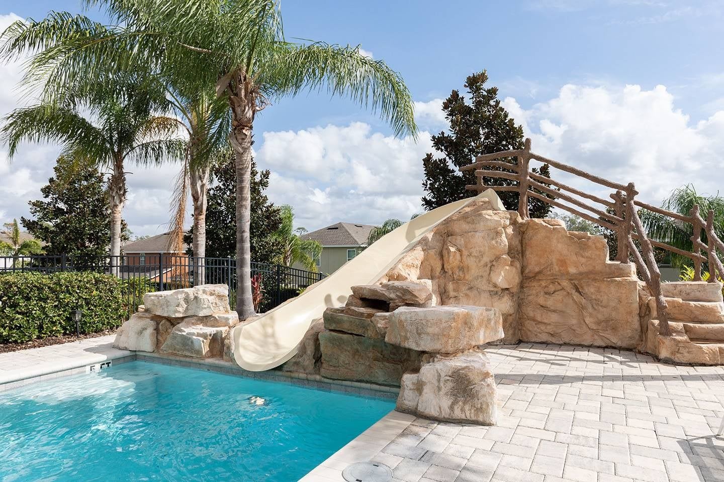 A swimming pool with a slide, surrounded by palm trees and a rock formation.