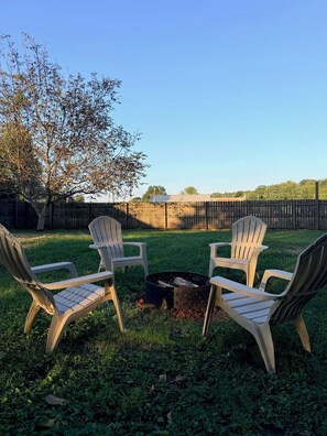 Ein Garten mit zwei Adirondack-Stühlen vor einem Feuerkorb.