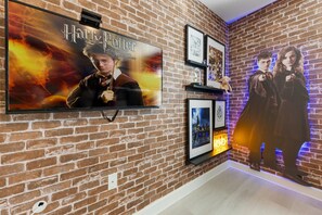 A brick wall with a flat-screen TV displaying a Harry Potter movie poster, framed pictures, and a shelf with memorabilia. - 4BR Championsgate Themed Rooms & Private Pool (Davenport)