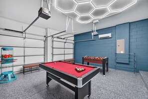 Ein Billardtisch mit roter Spielbahn, ein Kicker und ein Billardgestell mit Kugeln.