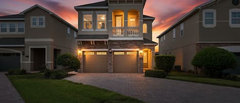 A two-story residential building with a central entrance, a covered front porch, and a driveway leading to the garage.