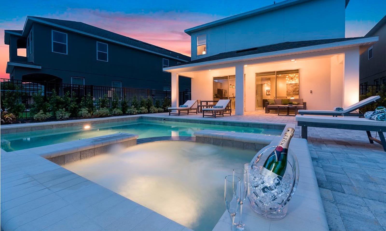 Een modern huis met een zwembad, lounge stoelen en een fles champagne.