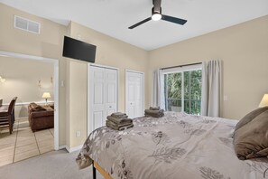 Ein Schlafzimmer mit einem Bett, einem Deckenventilator, einem Fenster mit Vorhängen und einer Tür.