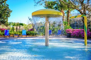 Ein Wasserspiel mit einer zentralen Säule und einer Fontäne, umgeben von blauen Stühlen und Grünpflanzen.