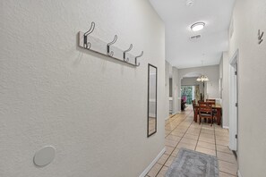 A hallway with a tiled floor, a rug, a wall-mounted light fixture, and a door leading to a dining area. - 3BR Condo for 8 at Bahama Bay Resort (Davenport)