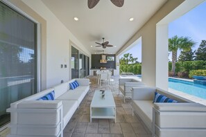 A modern outdoor living area with a pool, white furniture, and a ceiling fan. - 5BR Bear's Den Theater, Pool & Spa (Kissimmee)