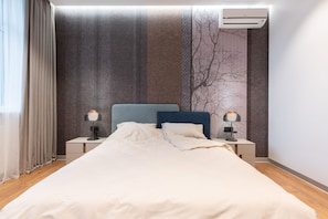 Una cama bien hecha con cabecera, dos lámparas de noche, aire acondicionado de pared y una ventana con cortinas.