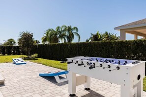 Ein Tischkicker auf einer gepflasterten Terrasse, im Hintergrund ein Hecke und Palmen.