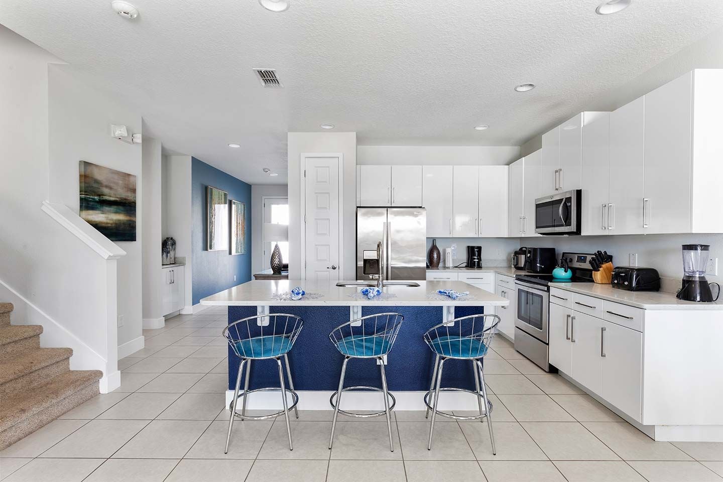 A modern kitchen with a central island, stainless steel appliances, and bar-style chairs.