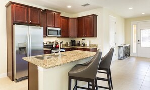 A modern kitchen with dark wood cabinets, stainless steel appliances, granite countertops, and two bar stools. - 7BR Encore Villa With Epic Game Loft & Pool (Kissimmee)