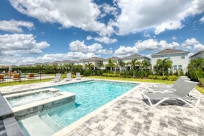 Ein Swimmingpool mit Liegestühlen und einem Whirlpool, umgeben von einer Einfriedung und Palmen.